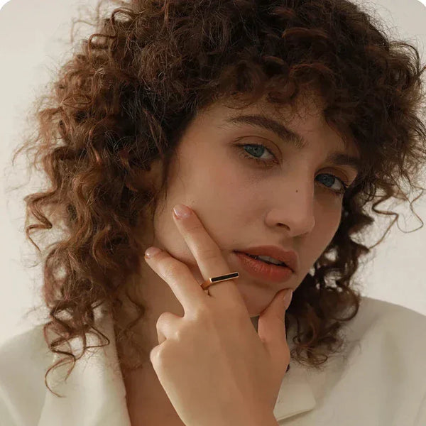 Woman in white blazer wearing minimalist gold-plated bar ring, posing with hand near face