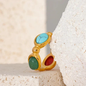 Gold-plated ring with red, green, and blue gemstones on textured stone background