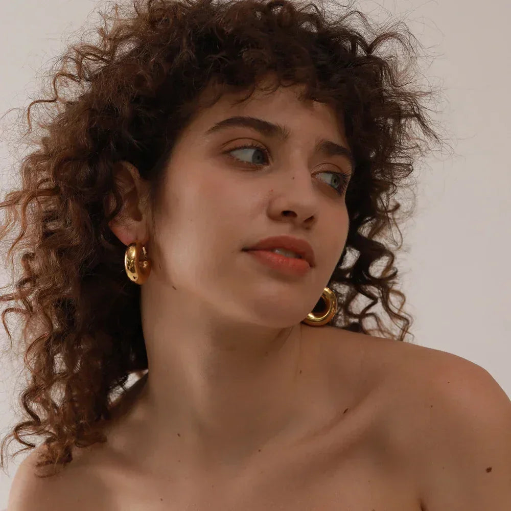 Woman with curly hair wearing large gold hoop earrings against a neutral background