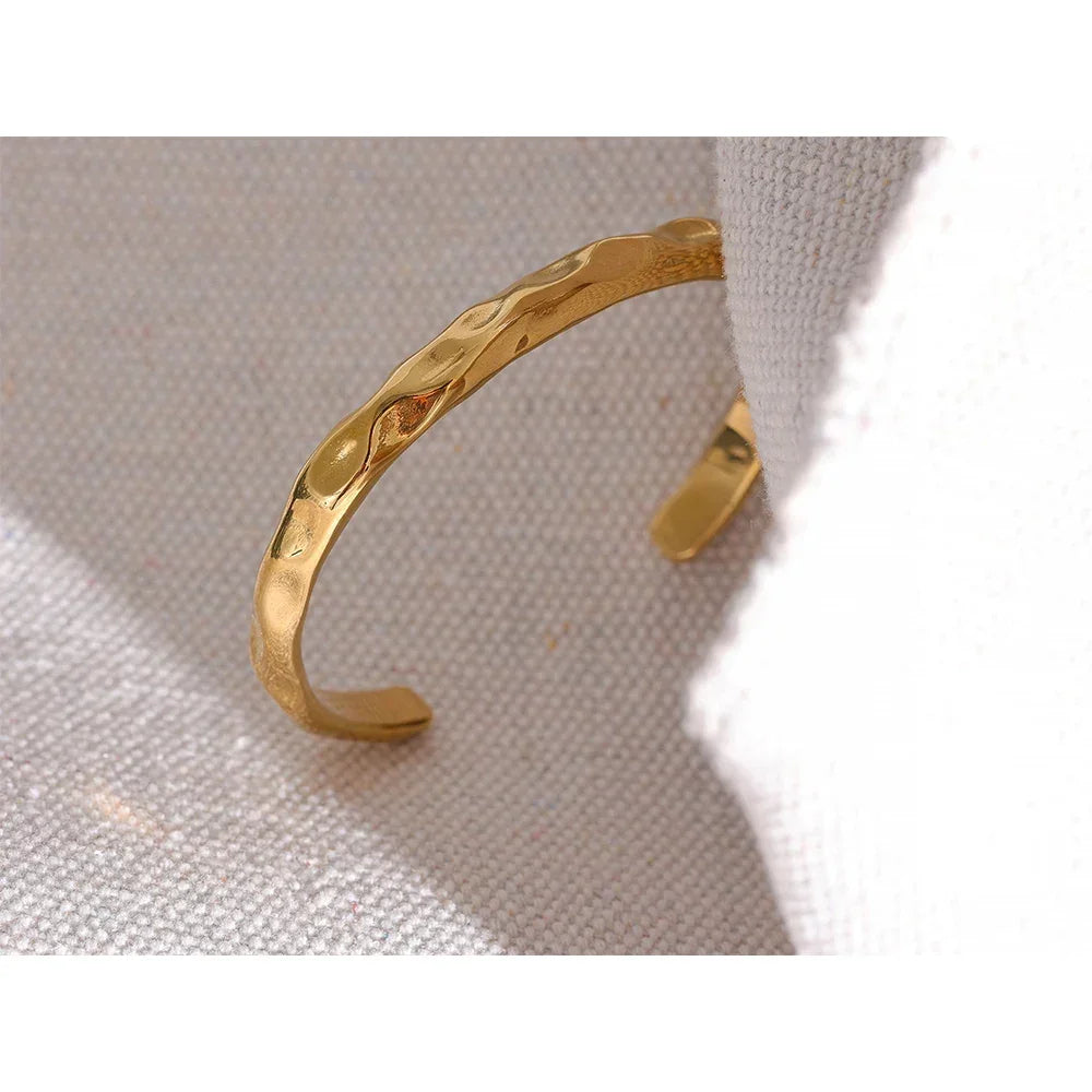 Hammered 18K gold-plated cuff bracelet on neutral textured fabric background