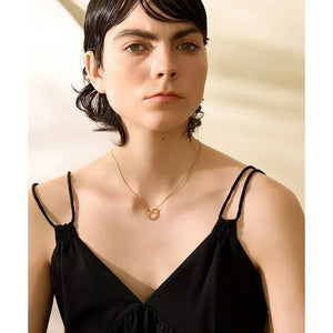 Woman wearing a gold-plated heart pendant necklace with a black spaghetti strap dress