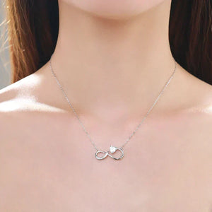 Silver infinity necklace with a heart detail on a model's neck.Glowing Heart Charm Necklace - TM & CO. JEWELS 