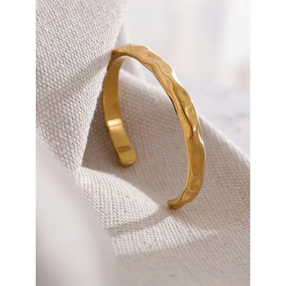 Textured gold-plated open bangle bracelet resting on a neutral fabric surface