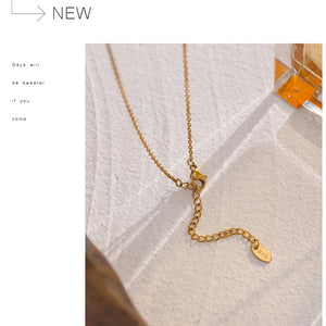 Gold necklace on a textured white surface with 'NEW' text above.