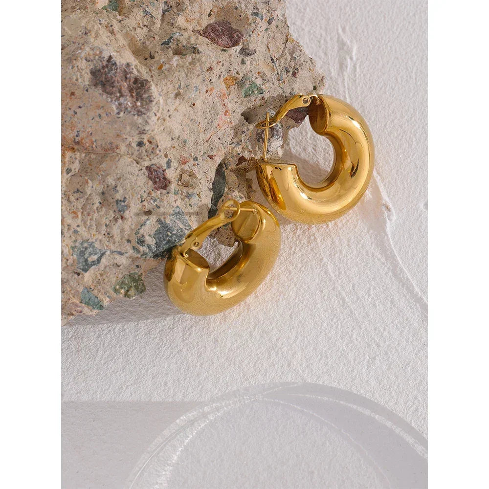 Chunky 18K gold-plated hoop earrings on textured stone background