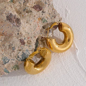Chunky 18K gold-plated hoop earrings on textured stone background