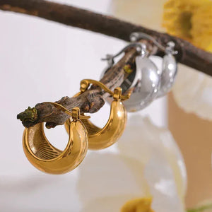 Gold and silver hoop earrings on a branch with soft floral background, elegant jewelry display
