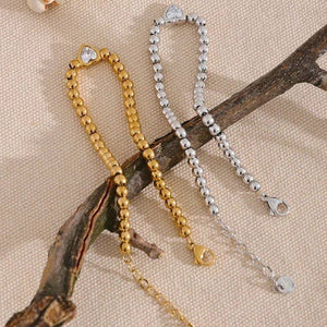 Gold and silver beaded bracelets with heart detail on beige fabric background