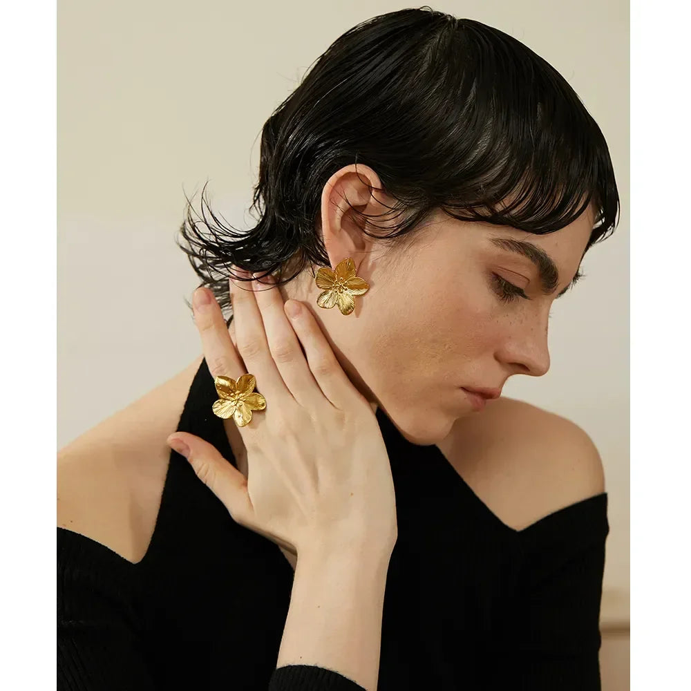 Woman wearing gold-plated floral earrings and matching statement ring, elegant jewelry