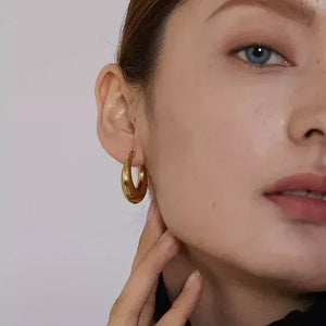 Woman wearing chunky gold-plated hoop earring, close-up on ear and hand