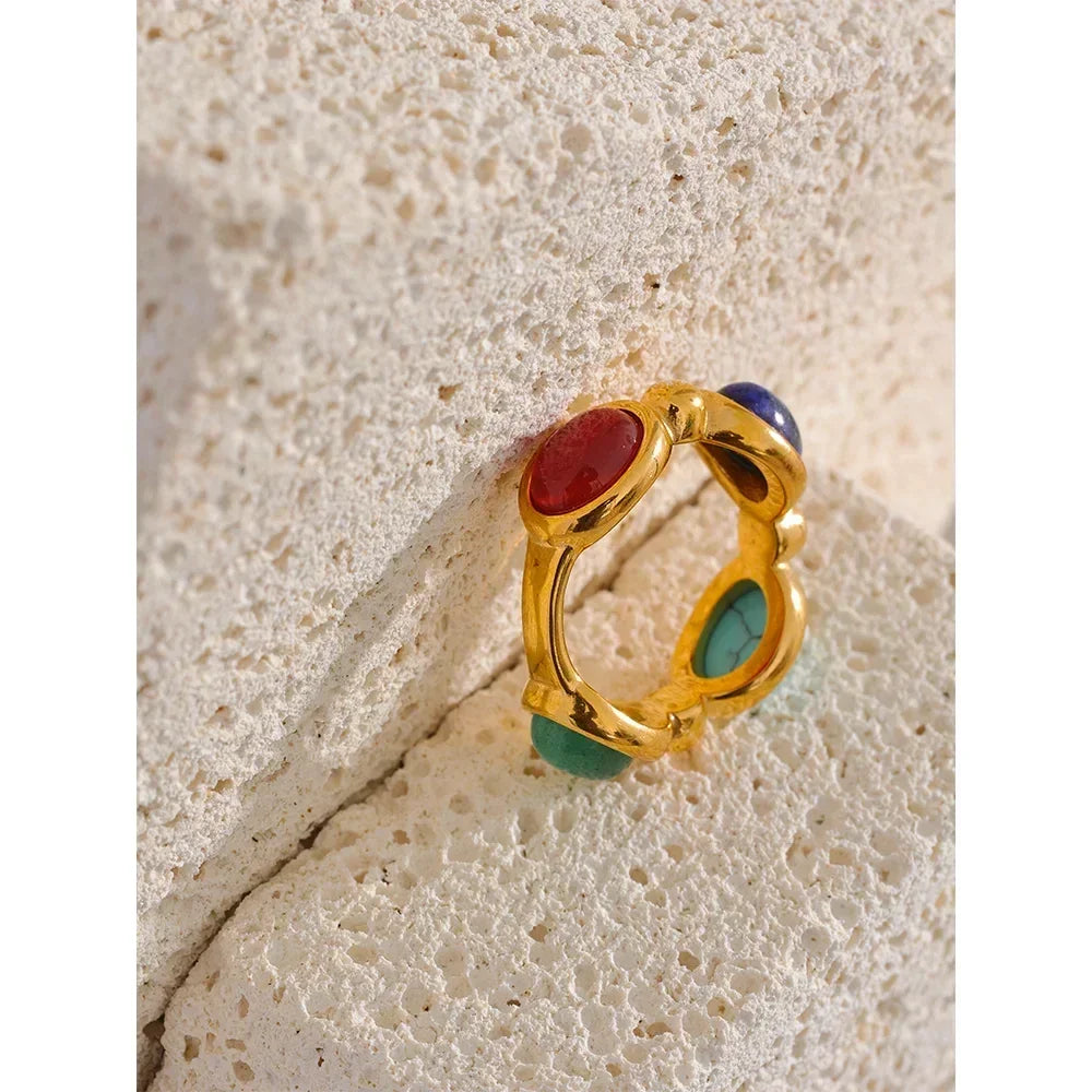 Gold-plated ring with red, green, and blue gemstones on textured stone background
