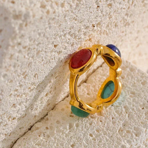 Gold-plated ring with red, green, and blue gemstones on textured stone background