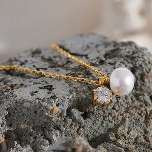18K gold-plated necklace with pearl and crystal pendant on textured stone