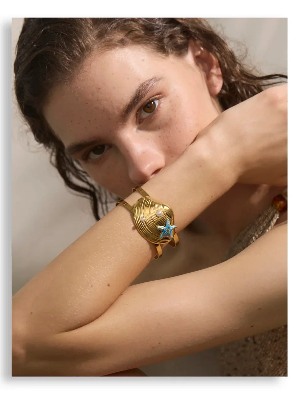 Woman wearing a gold bracelet with a star charm against a neutral background