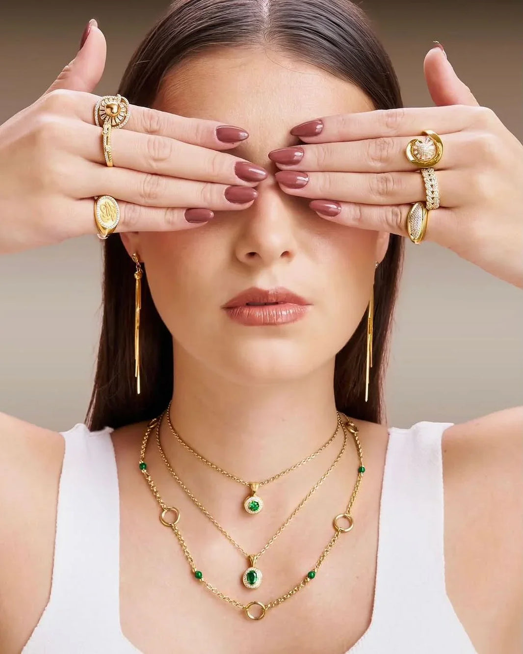Woman wearing gold jewelry with green gemstones, covering her eyes.
