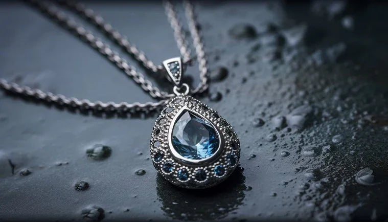 Silver teardrop pendant with a blue gemstone on a dark surface with water droplets
