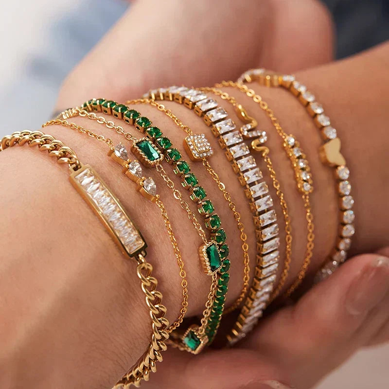 Multiple gold bracelets with green and clear stones on a wrist.